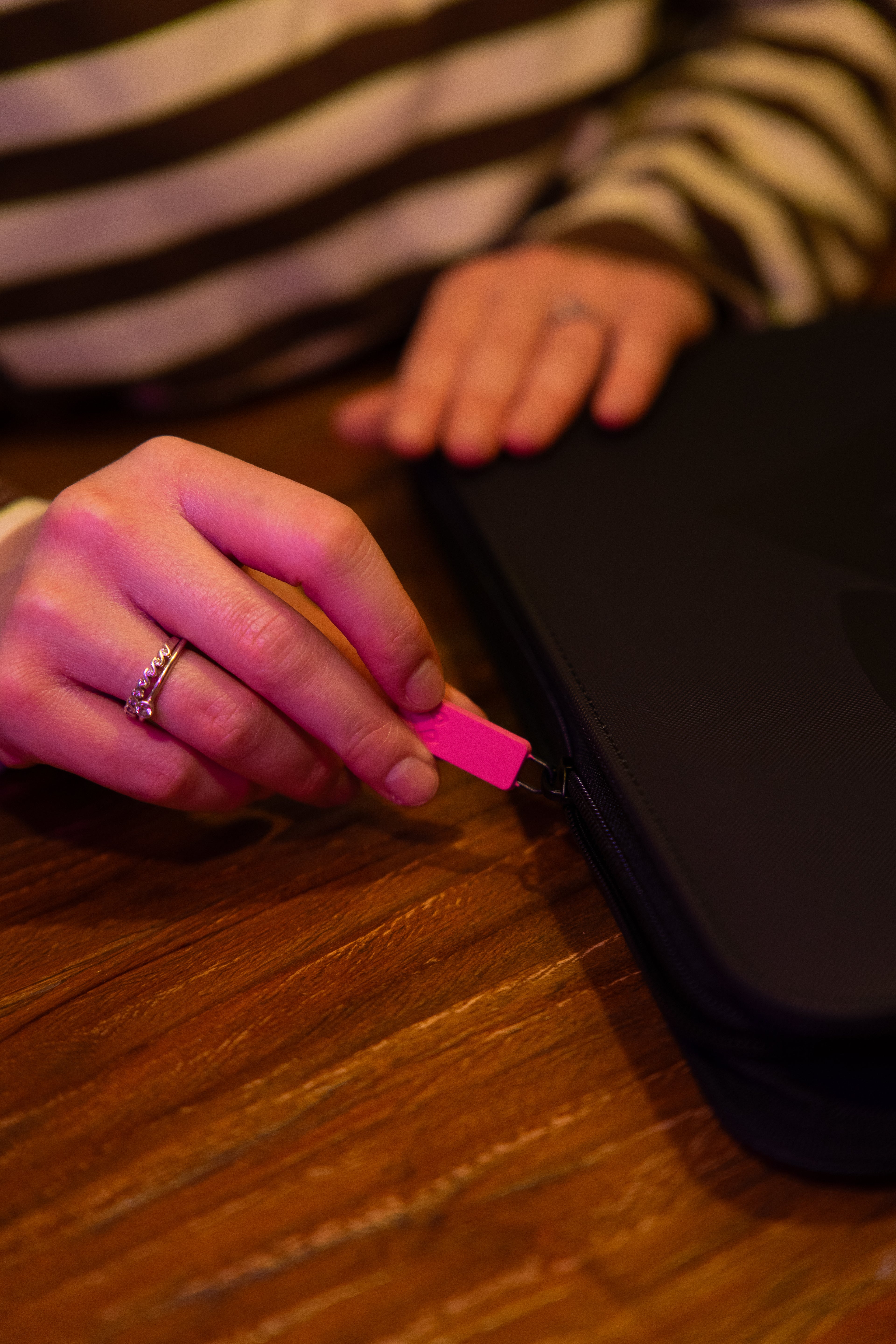 Hand die de ritssluiting van een zwarte kaartenmap opent op een houten tafel.