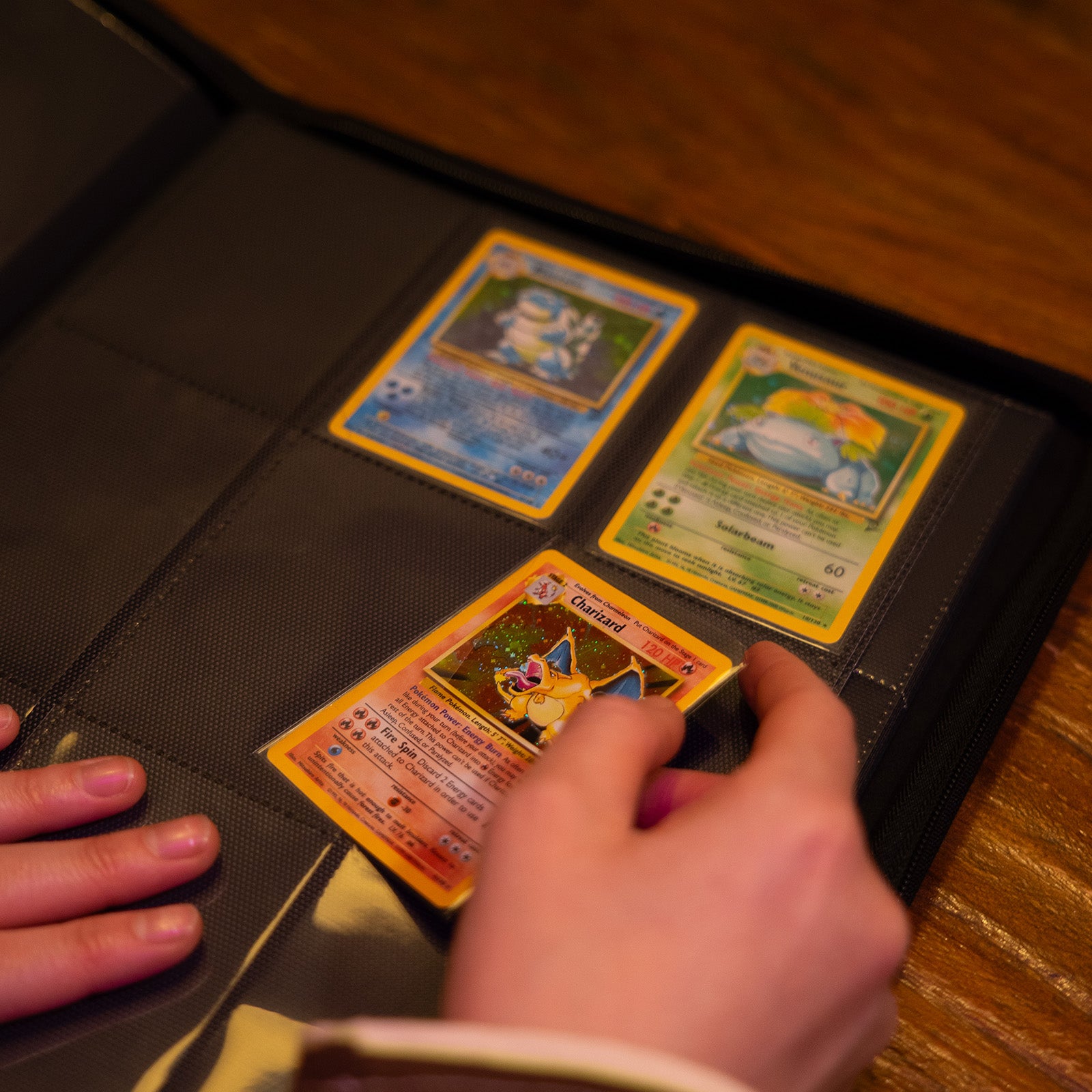 hand die een Charizard Pokémonkaart in een Luxafox binder stopt